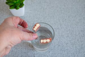 A,Hand,Removes,A,Partial,Denture,From,A,Glass,Of water